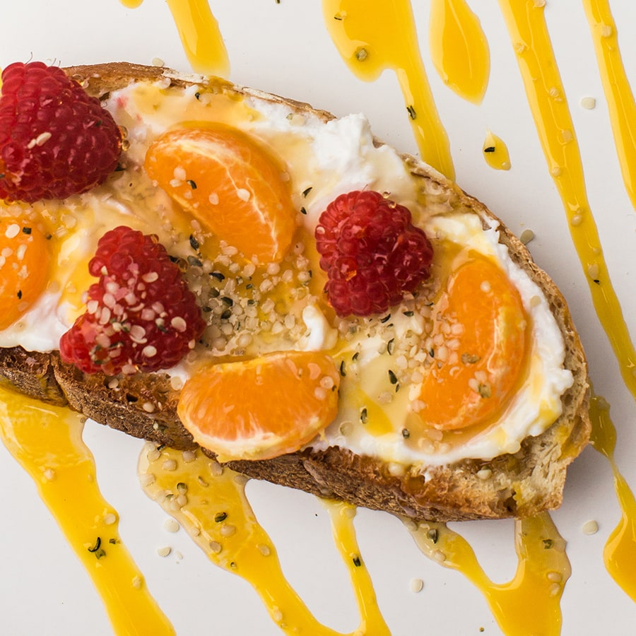 Slice of toast topped with yogurt spread, clementines, raspberries, & mango