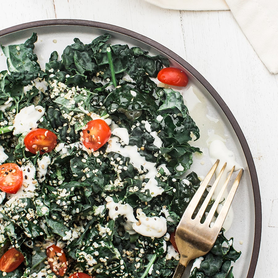 A plate filled with farmhouse kale salad topped with tomatoes and a creamy dressing.