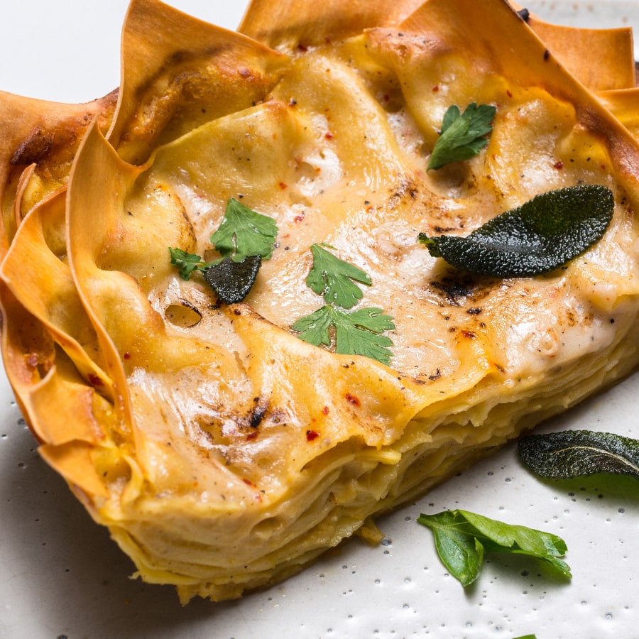Casserole dish filled with butternut squash and sage lasagna topped with fresh herbs