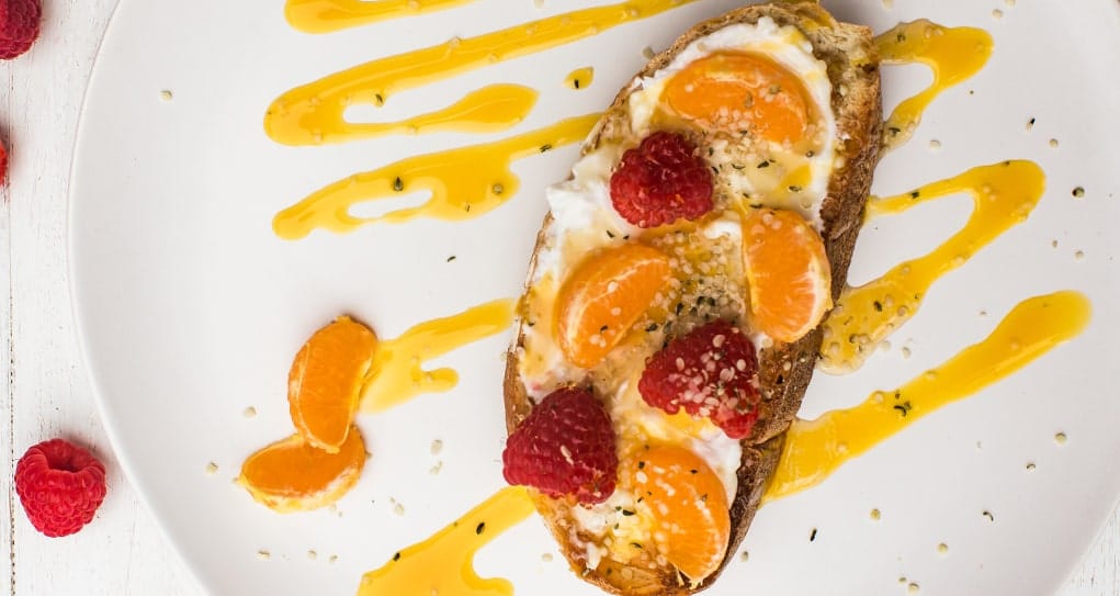 Slice of toast topped with yogurt spread, clementines, raspberries, & mango