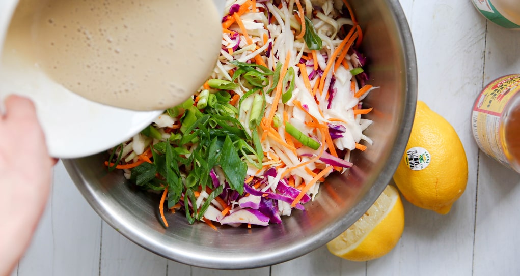 Tangy vegan dressing being poured over a bowl of shredded coleslaw veggies