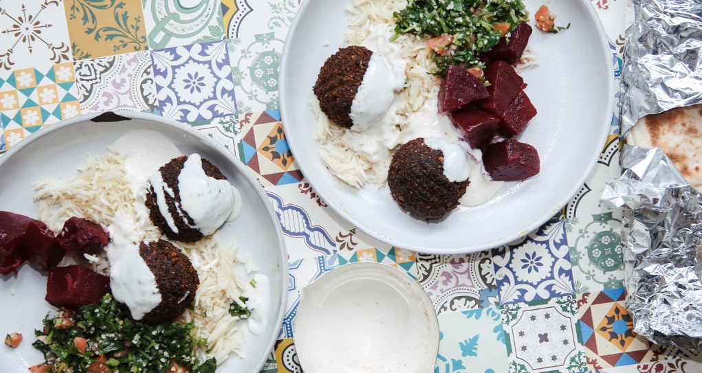 Two plated with falafel, basmati rice, roasted beets and tabbouleh topped with a white sauce