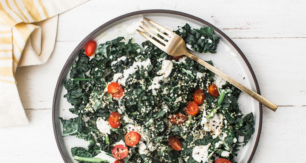 A plate filled with farmhouse kale salad topped with tomatoes and a creamy dressing.