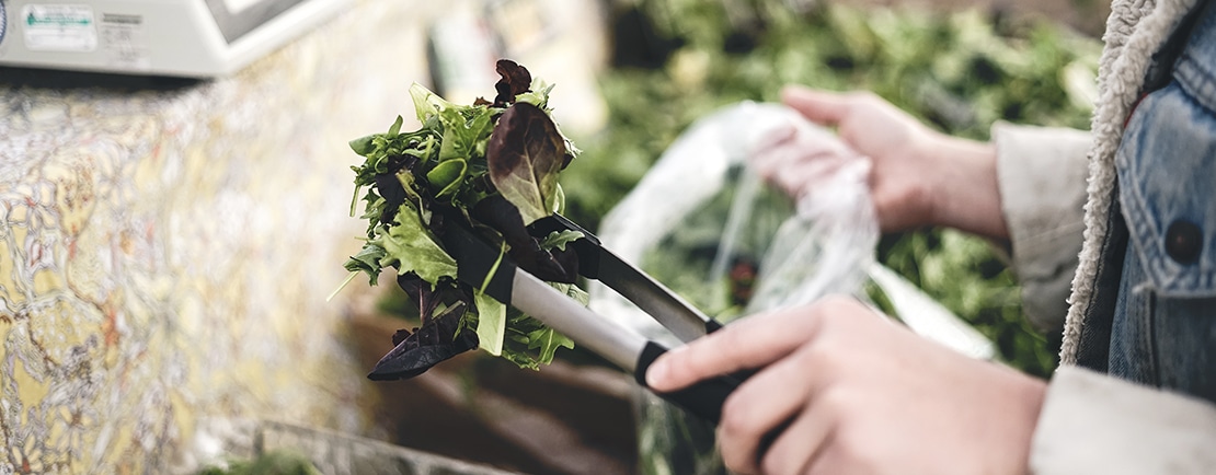 Close up of someone putting lettuce into a bag at a farmer's market.
