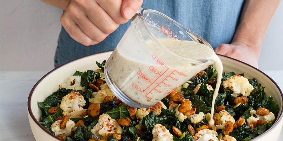 Dressing being poured ove a bowl of the Roasted White Bean, Kale and Cauliflower Salad.