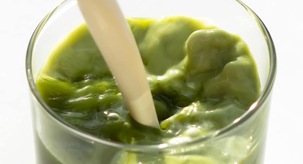 Closeup of Cashewmilk being poured into a glass of iced vanilla bean matcha latte