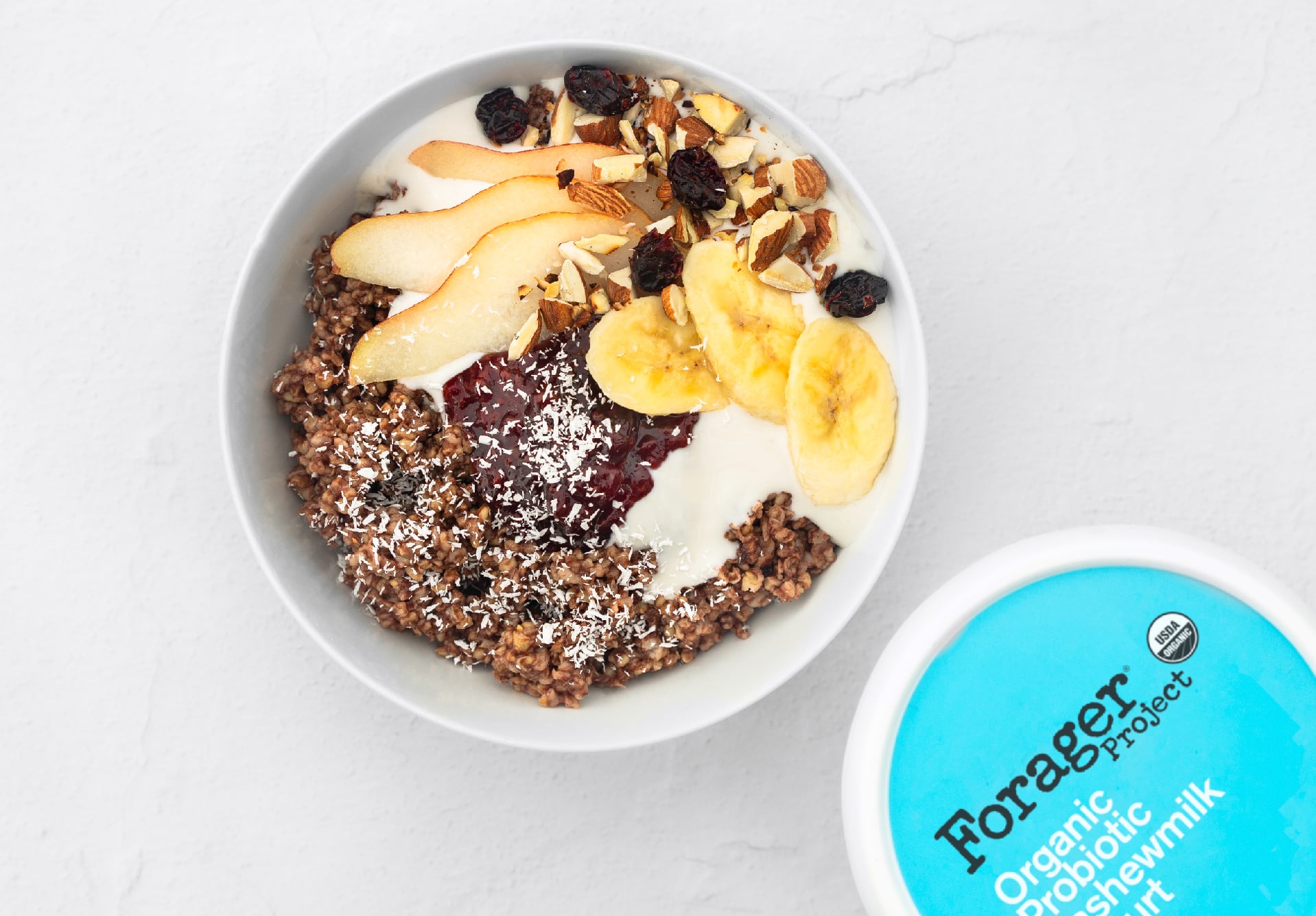 Breakfast bowl topped with pears, dried fruit, nuts, jam and shredded coconut.