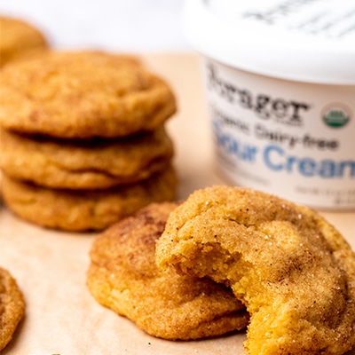 Stack of pumpkin cookies on parchment paper next to a tub of Forager project vegan sour cream.