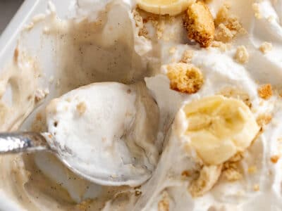 Close up of creamy vegan banana pudding topped with whipped cream, cookie crumbles and slices of banana.