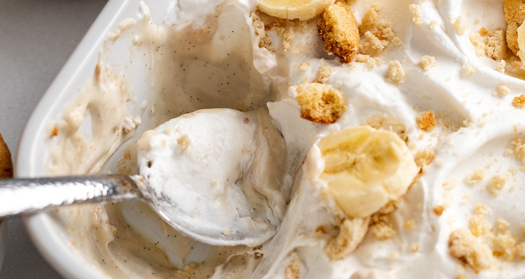 Close up of creamy vegan banana pudding topped with whipped cream, cookie crumbles and slices of banana.