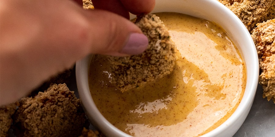 Close up of crispy vegan nugget being dipped in a vegan honey mustard sauce.
