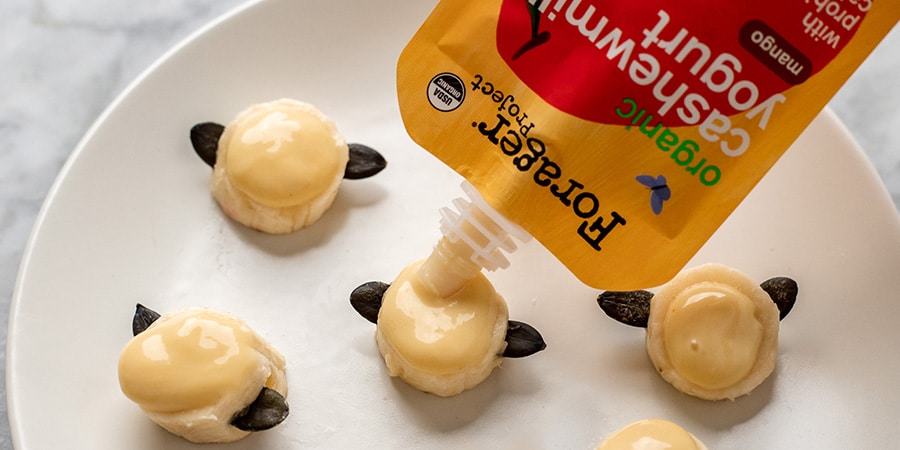 Squeezing mango yogurt from pouch on banana slices to make bee shaped treats.