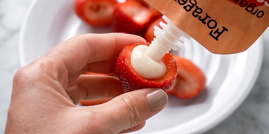 Strawberries being filled with yogurt from a pouch.