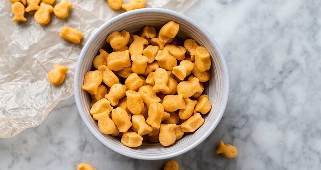 Vegan goldfish crackers in a bowl with some sprinkled on the counter.