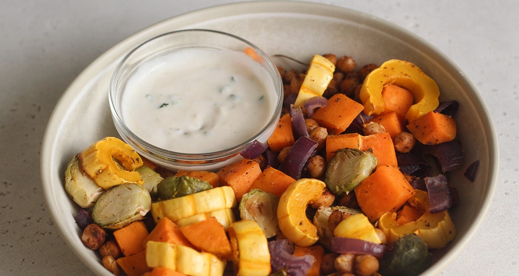 Bowl filled with fall vegetables paired with a garlic sauce.