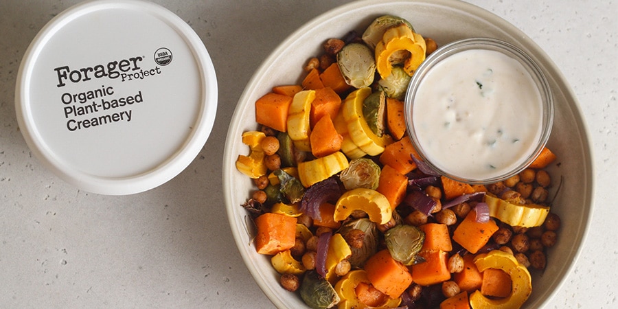Top view of a large bowl of fall vegetables with a small side bowl of garlic sauce.