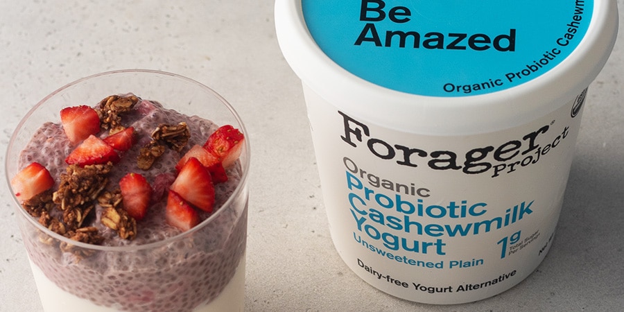 Close up of a glass of berry chia pudding sitting next to a tub of Forager Project Unsweetened Plain Yogurt.