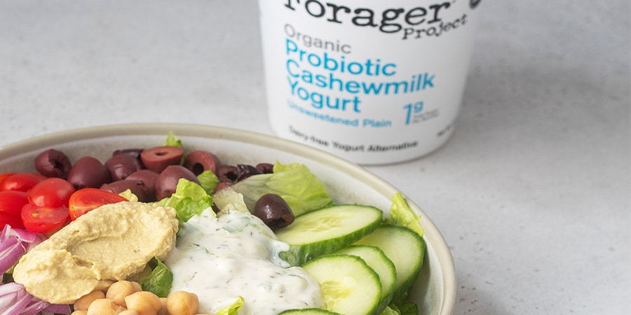 Close up of a vegan Mediterranean Bowl sitting next to a tub of Forager Project Unsweetened Plain Cashewmilk Yogurt.